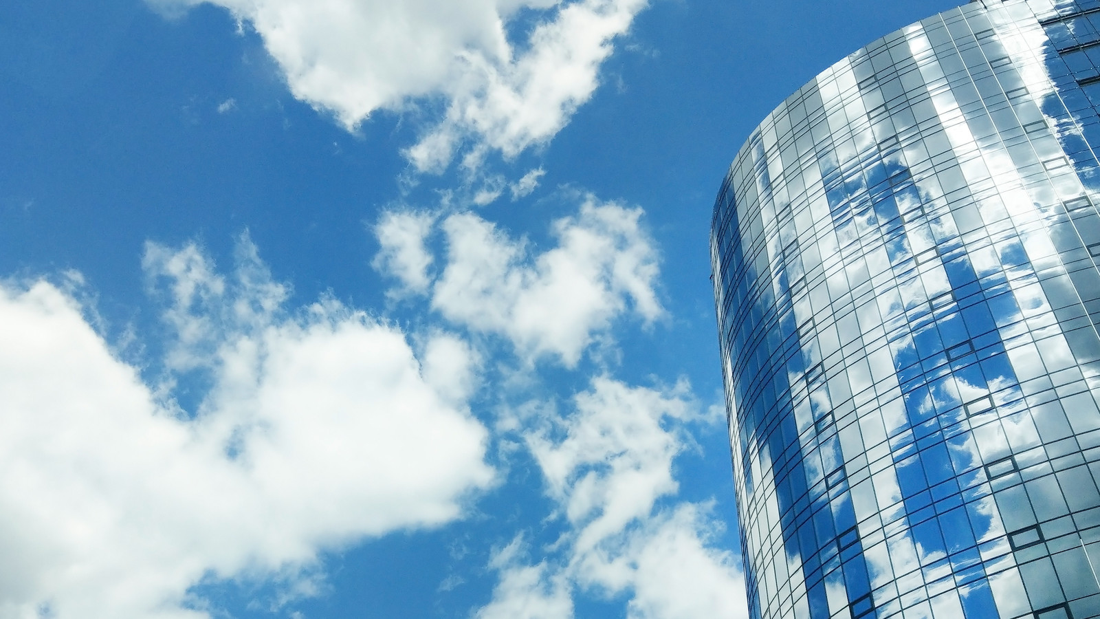 Round mirrored glass of modern office center building.Clear blue sky and reflection in windows