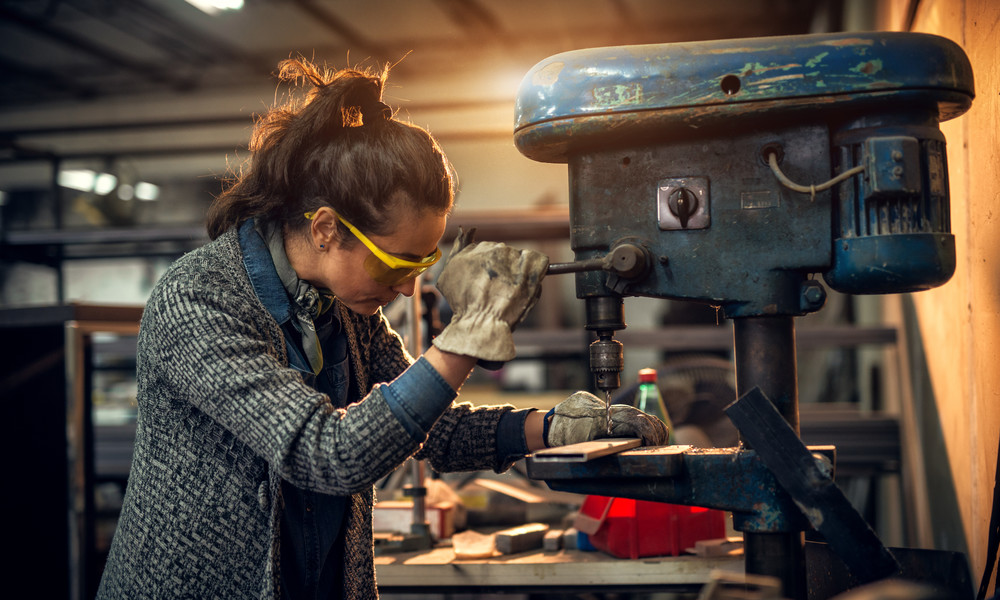 Portrait view of focused serious middle aged professional female carpentry working with an electric drill in the workshop.